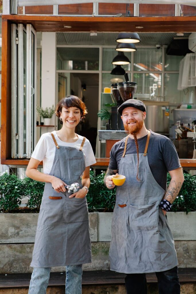 Positive man with cup of coffee and woman with filter holder standing on terrace of modern cafe during work break